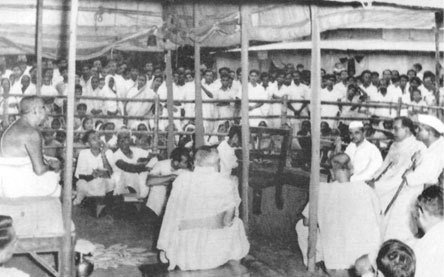 Thakur seated among a large gathering under a tent, with visitors seated before him
