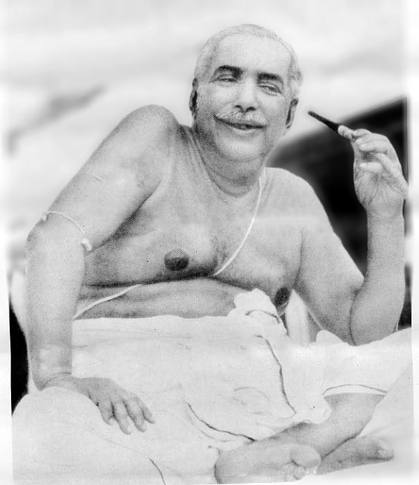 Thakur Anukulchandra in his later years, seated and smiling, a pipe in his hand