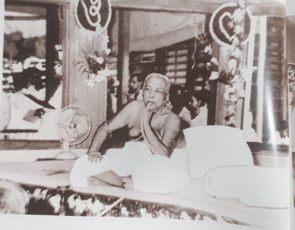 Thakur Anukulchandra seated on a bed, with people gathered around him