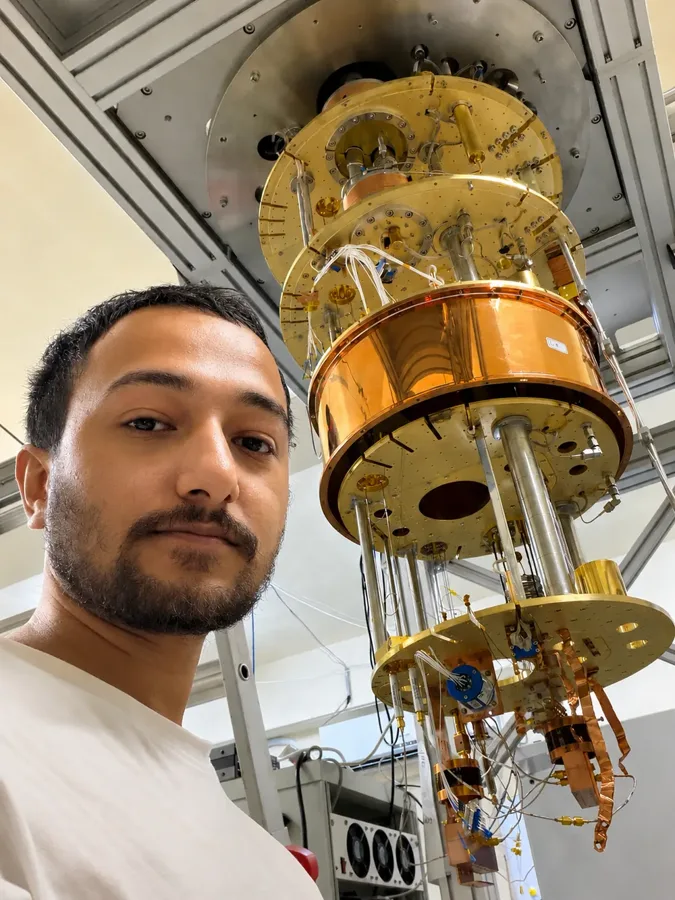 Souvik Ghosh beside an open dilution refrigerator: gold-plated plates stacked one below another, hung with wiring and copper parts
