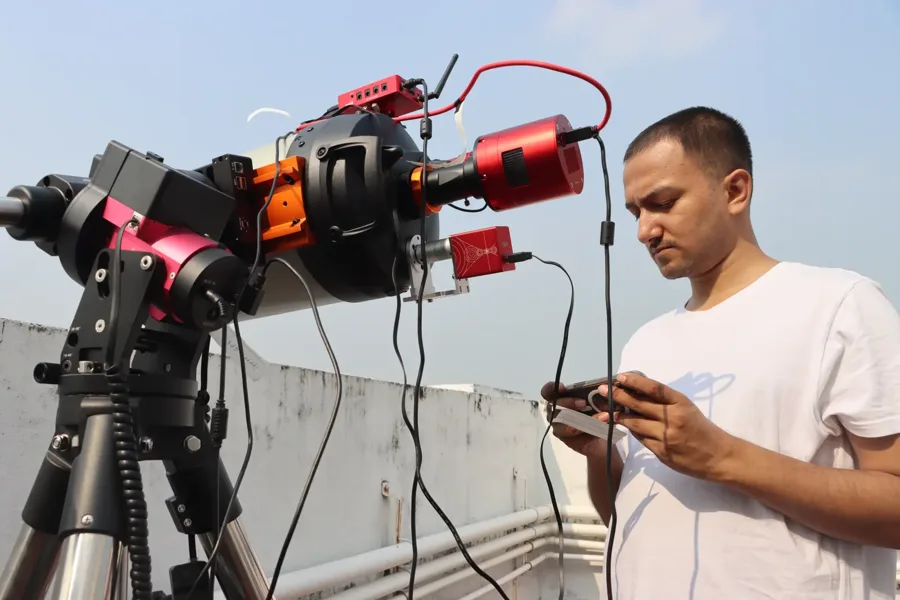 The Purākaash telescope on a rooftop in daylight, its cameras and cables attached, with Souvik Ghosh beside it holding the hand controller